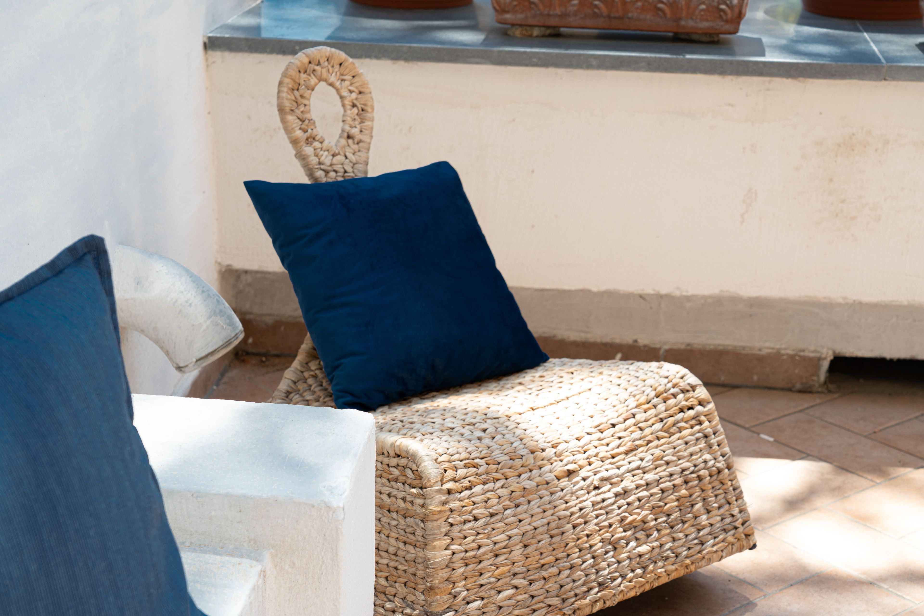 Wicker furniture with a blue cushion, a stone bench, and a wall with a decorative element.