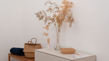 Quarto com um banco de madeira, um armário branco e uma prateleira com galhos decorativos e uma cesta trançada.