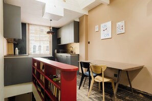 A compact kitchen with modern appliances, a dining area with a table and chairs, and a bookshelf. - Sublime 1BDR Coach House Conversion in Hackney (London)