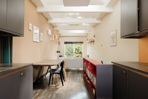 A modern kitchen with a dining area, wooden flooring, and a view of greenery outside. - Sublime 1BDR Coach House Conversion in Hackney (London)