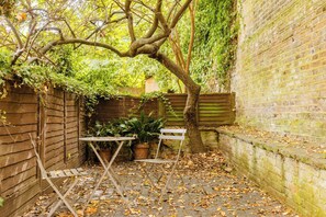 A garden with a table and chairs, surrounded by brick walls and a wooden fence. - Sublime 1BDR Coach House Conversion in Hackney (London)