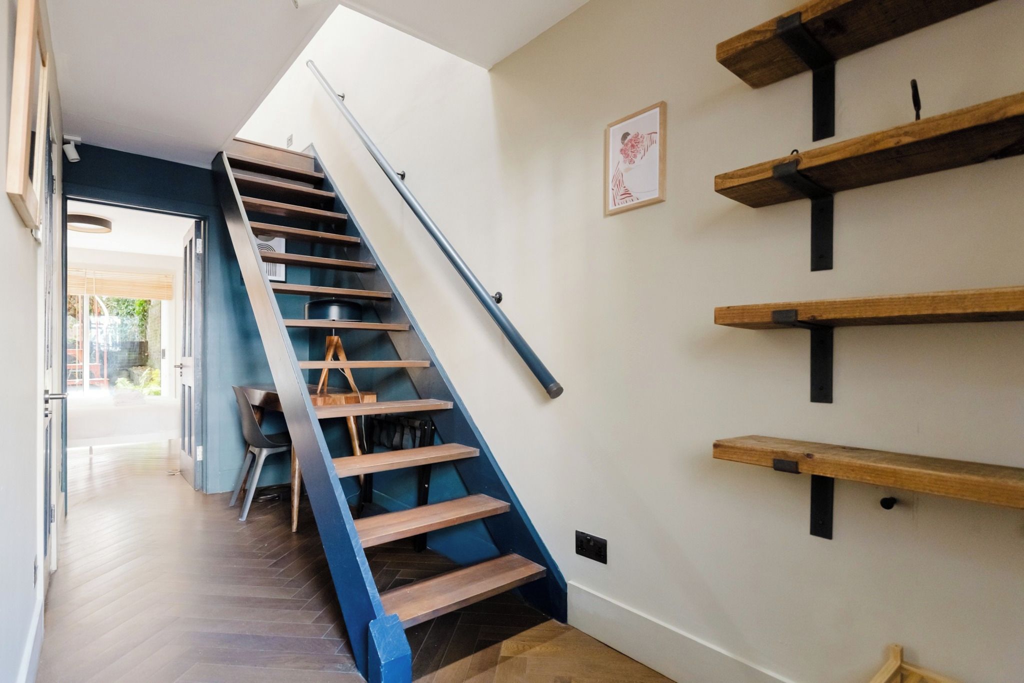 A staircase with wooden steps and blue handrails, leading to a room with a chair and a table.