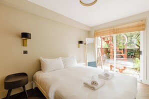 A hotel room with a bed, two wall-mounted lamps, a small table, and a view of an outdoor area with a wooden structure. - Sublime 1BDR Coach House Conversion in Hackney (London)