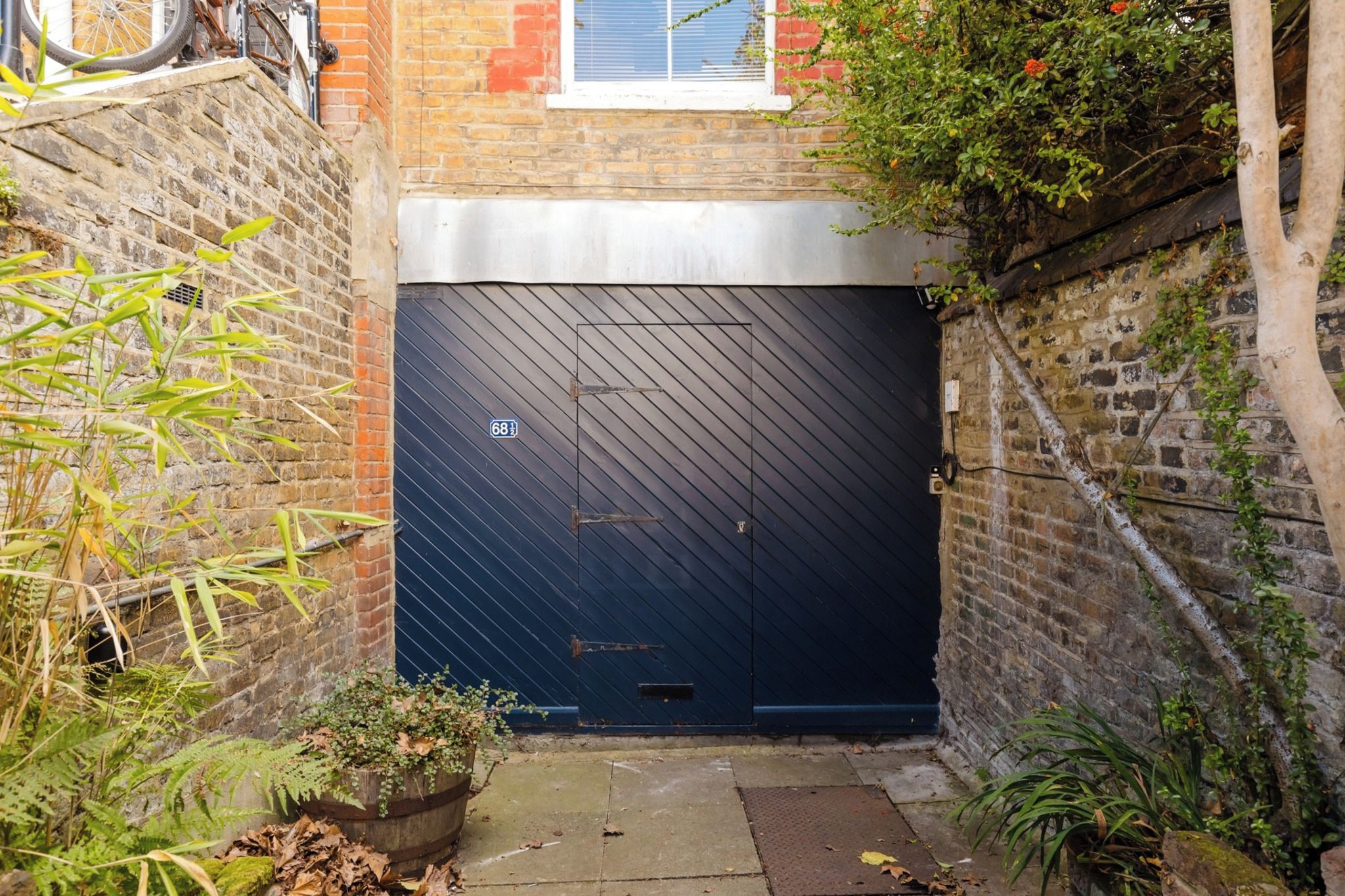 A dark blue garage door with a number plate, a brick wall, and some greenery.