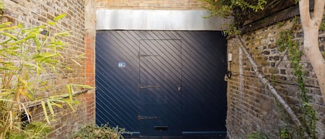 A dark blue garage door with a number plate, a brick wall, and some greenery.