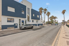 Een modern gebouw met een auto ervoor, palmbomen langs de straat en een heldere lucht.