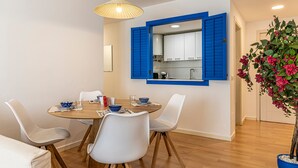Uma sala de jantar com uma mesa redonda, cadeiras brancas e um espelho com moldura azul acima.