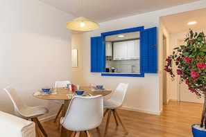 Een eetruimte met een ronde tafel, witte stoelen en een spiegel met blauwe lijst erboven.