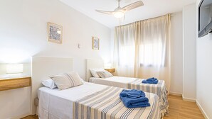 Quarto de hotel com duas camas, um ventilador de teto, televisão e janela com cortinas.