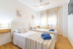 Een hotelkamer met twee bedden, een plafondventilator, een televisie en een raam met gordijnen.