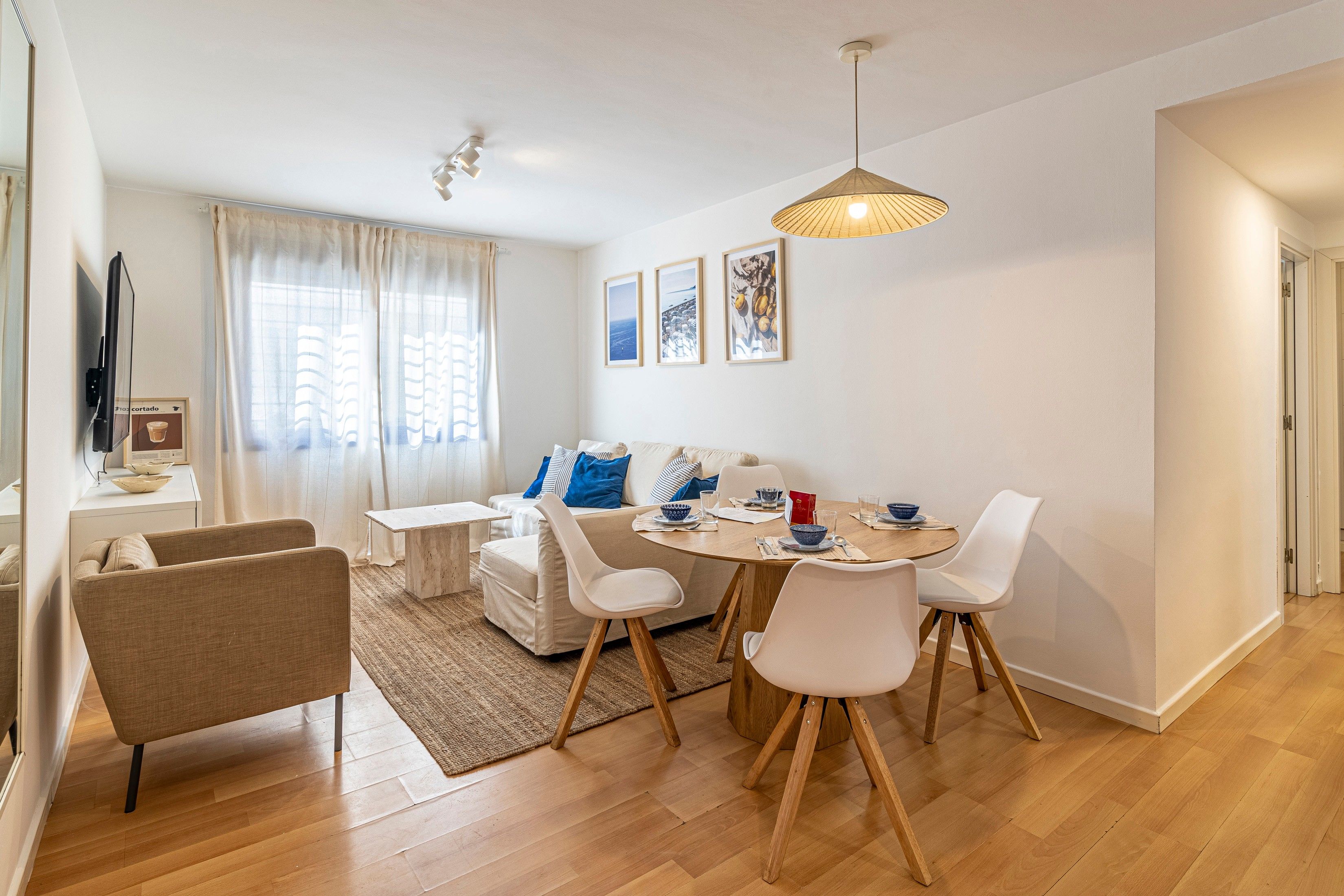 A modern dining area with a round table, white chairs, and a hanging light fixture.