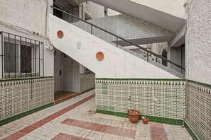 Uma escadaria com parede revestida de azulejos brancos e verdes, corrimão de metal e um vaso de planta.