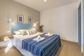 Quarto bem organizado com cama, almofadas, mesa de cabeceira e luminárias fixadas na parede.