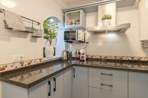 Et moderne køkken med hvide skabe, en granitbordplade, en elkedel, en kaffemaskine og en potteplante.