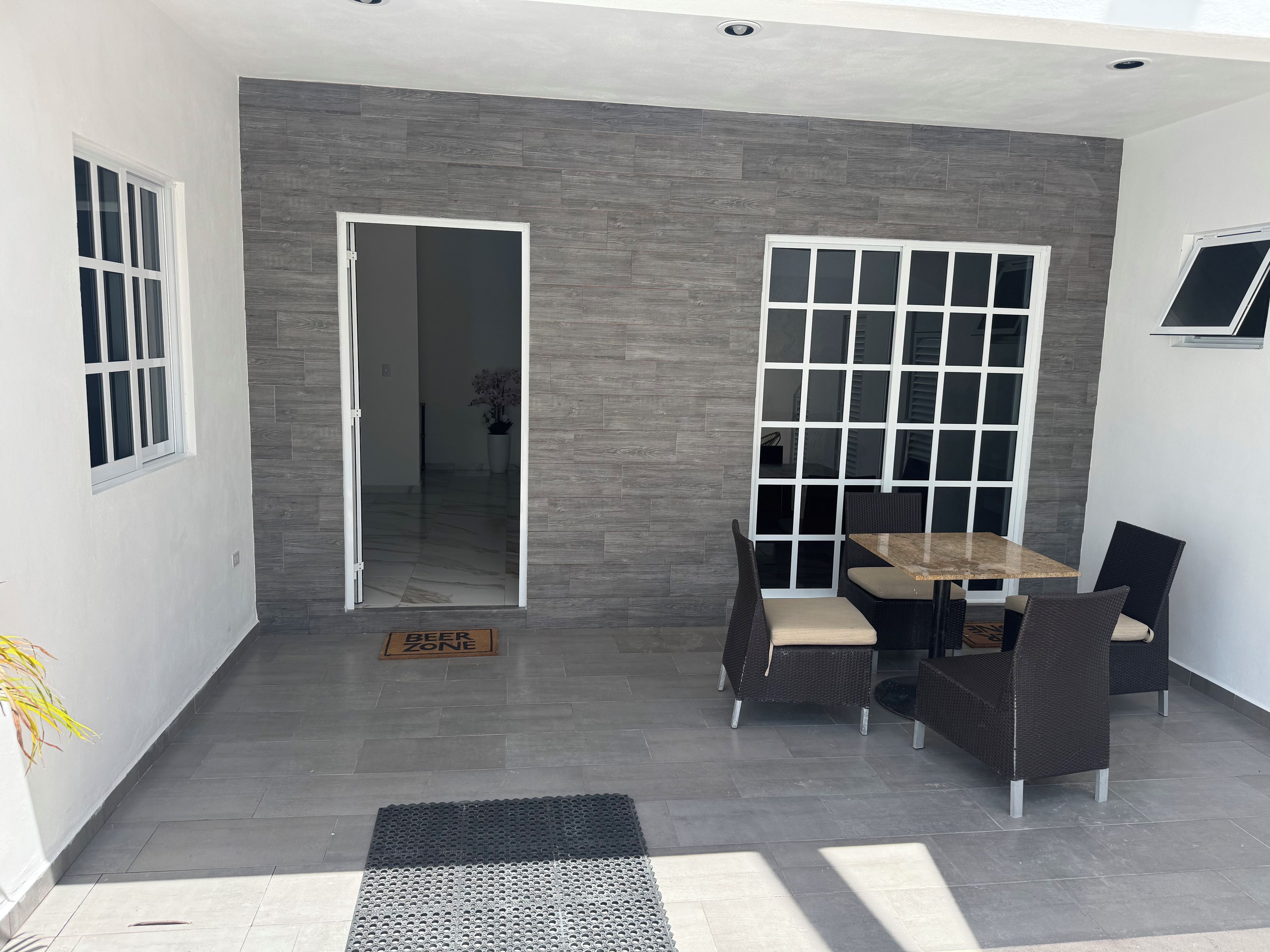 Ein moderner Patio-Bereich mit Esstisch und Stühlen, einer Tür zu einem Innenraum und einem kleinen Topfpflanzen.