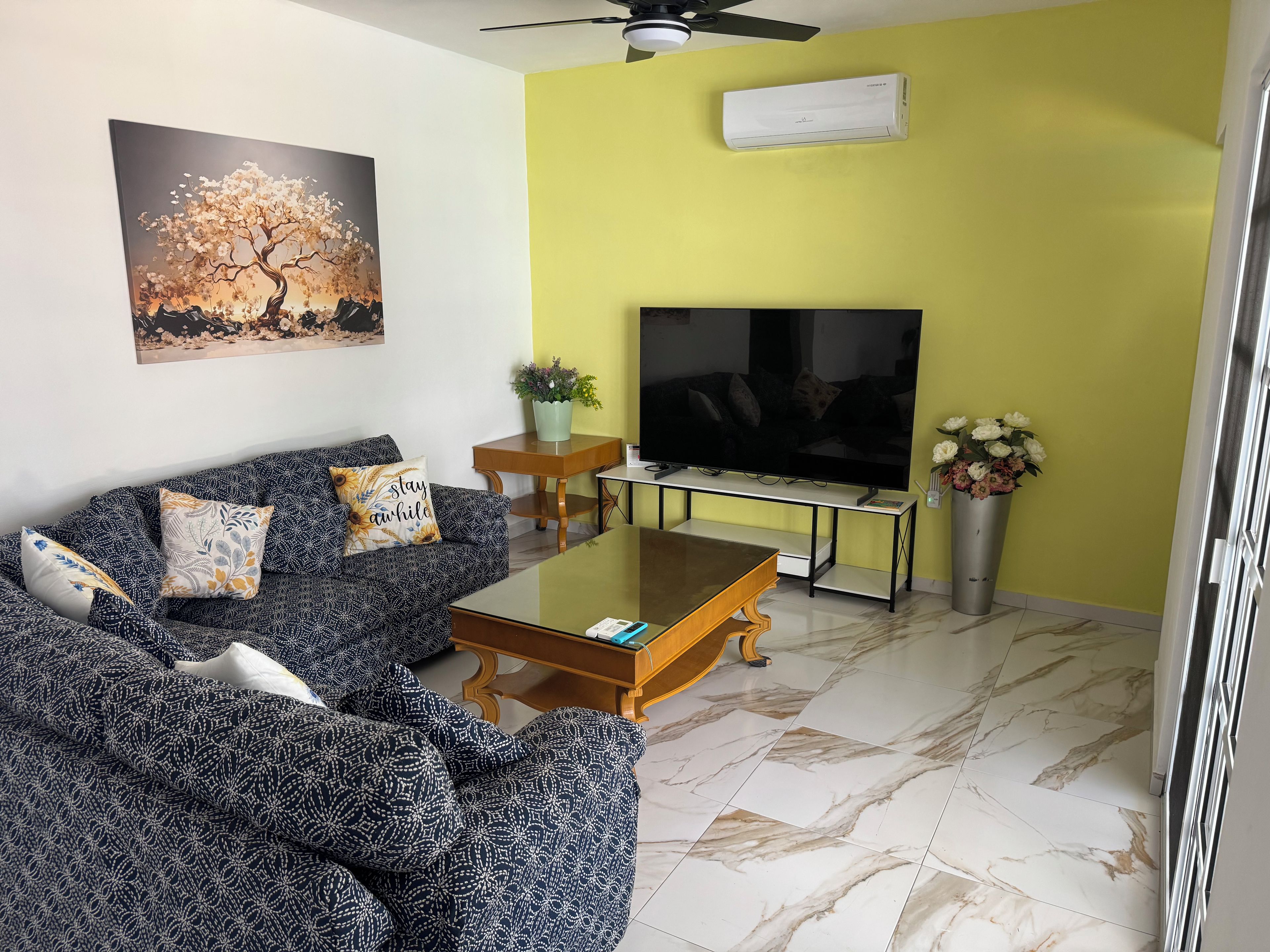 Uma sala de estar com sofá, mesa de centro, televisão e um quadro na parede.