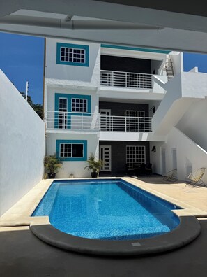 A modern two-story building with a swimming pool, outdoor seating, and a clear blue sky. - Stylish 2BR/2.5 BA Cancún Getaway with Pool, AC & Full Kitchen (Cancún)