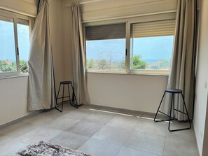 Een kamer met twee ramen en uitzicht op zee, plus twee zwarte krukken.