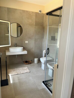A modern bathroom with a glass shower enclosure, a round mirror, a white sink, and a toilet. - SARACENA Realmonte, home to the Scala dei Turchi—a great destination for families and friends (Realmonte)