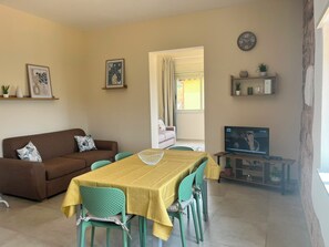 A living room with a sofa, a dining table with chairs, a television, and a wall clock. - SARACENA Realmonte, home to the Scala dei Turchi—a great destination for families and friends (Realmonte)