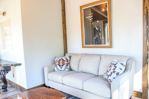 A living room with a sofa, two patterned pillows, a wooden coffee table, a mirror, and a wall-mounted light fixture. - Historic Weston Farmhouse - Private Countryside Escape (Weston)