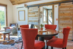 A room with a wooden ceiling, a large window, a dining table with chairs, and a leather sofa.