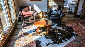 A room with leather armchairs, a wooden coffee table, a patterned rug, and a rustic wooden floor.