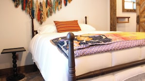 A bed with a quilt, a wooden headboard, a bedside table, and a wall with hanging items.