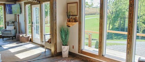 A spacious room with large windows, a wooden ceiling, and a cozy seating area with a rug and a plant.