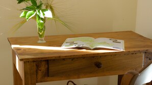 Uma escrivaninha de madeira com um vaso de plantas verdes, um livro aberto e uma cesta de vime.