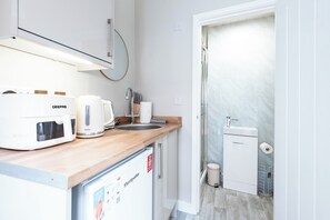 Une cuisine compacte équipée d’une machine à café Breville, d’un évier et d’un petit réfrigérateur.