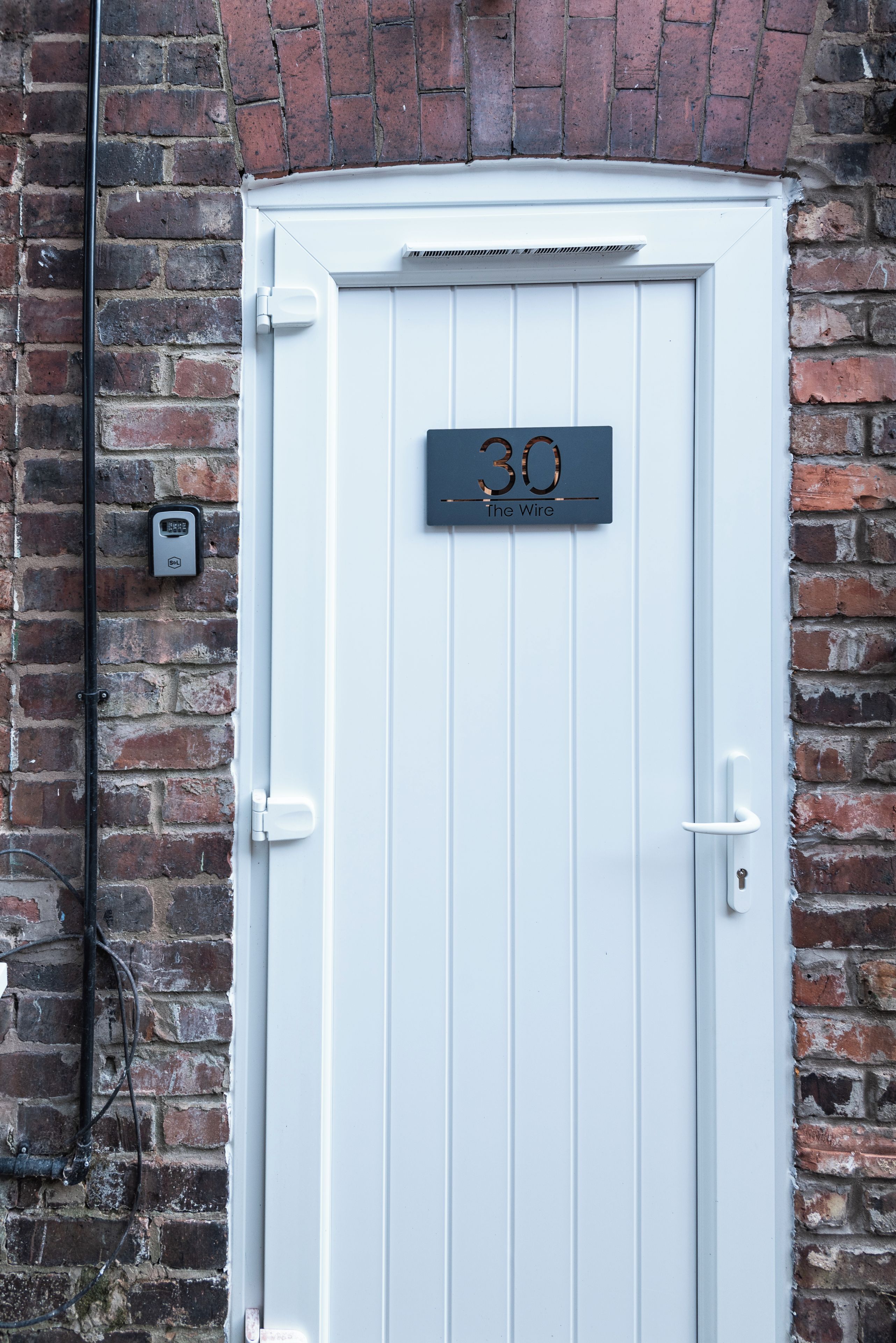 A white door with a number plate reading '30 The Wire' against a brick wall.