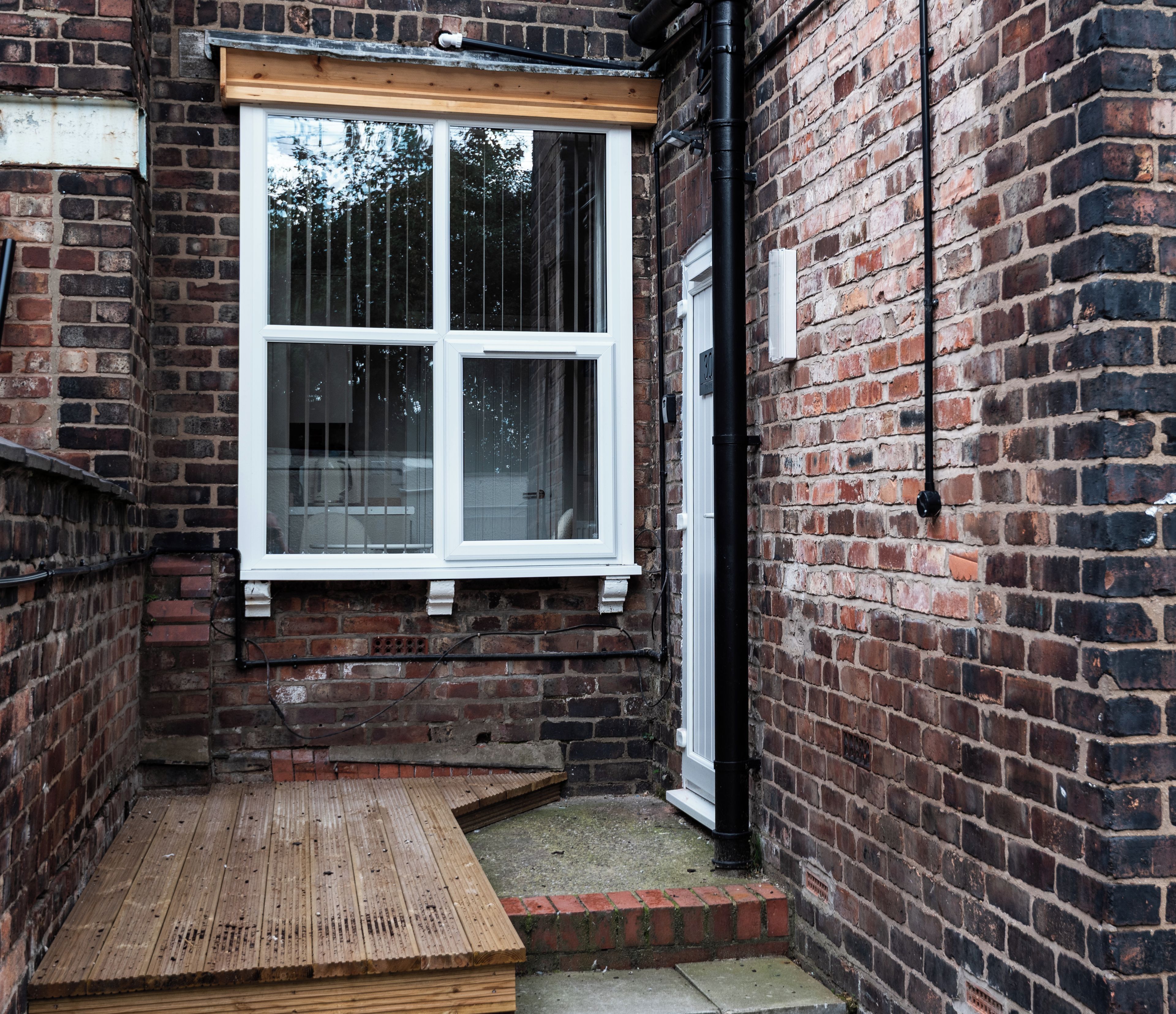 A narrow alleyway with a wooden deck leading to a white-framed window.