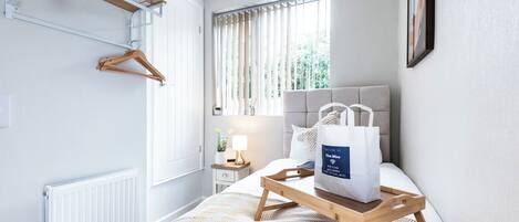 Habitación de hotel con cama, mesita de noche con lámpara, perchero y ventana con cortinas.