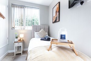 Une chambre d’hôtel avec un lit, une table de chevet, une lampe, une fenêtre avec des stores et un tableau au mur.