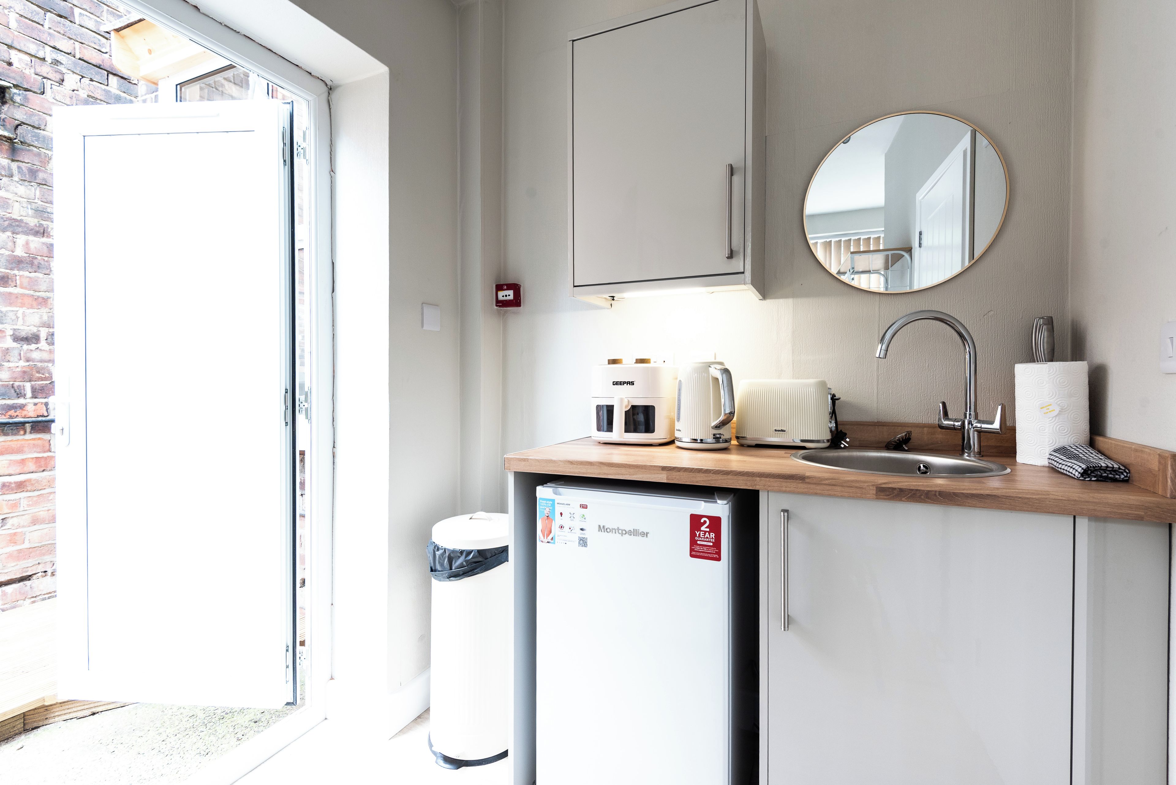 A compact kitchenette with a microwave, kettle, and sink.