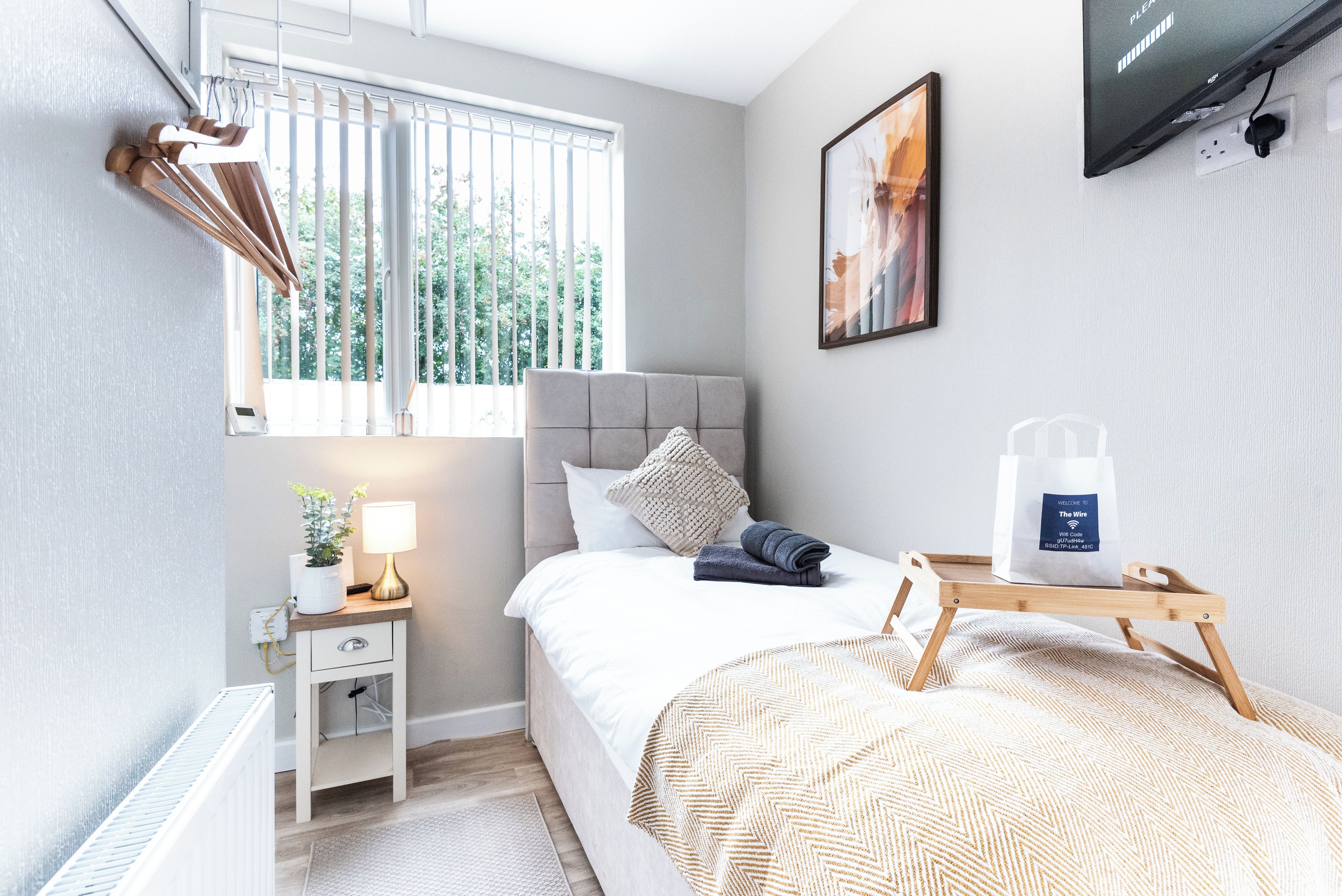 Une chambre moderne avec un lit, une table de chevet, une lampe et une fenêtre avec des stores.