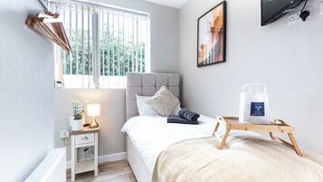 Une chambre moderne avec un lit, une table de chevet, une lampe et une fenêtre avec des stores.