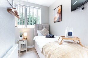 Une chambre moderne avec un lit, une table de chevet, une lampe et une fenêtre avec des stores.
