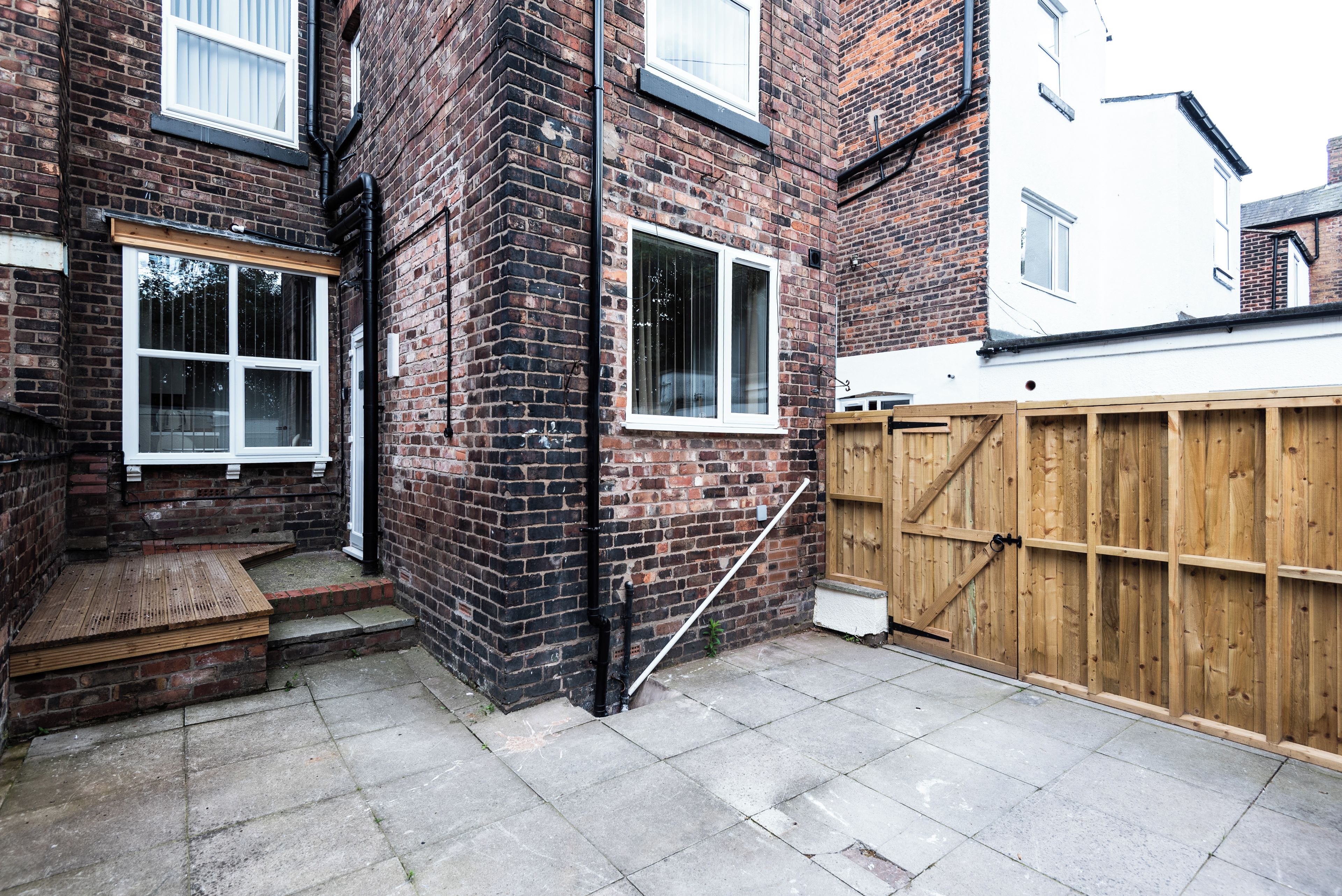 A brick house with a wooden fence, a small wooden bench, and a paved patio.