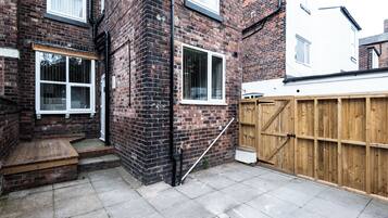 A brick house with a wooden fence, a small wooden bench, and a paved patio.