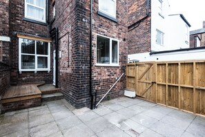 Ein Backsteinhaus mit Holzzaun, einer kleinen Holzbank und einer gepflasterten Terrasse.