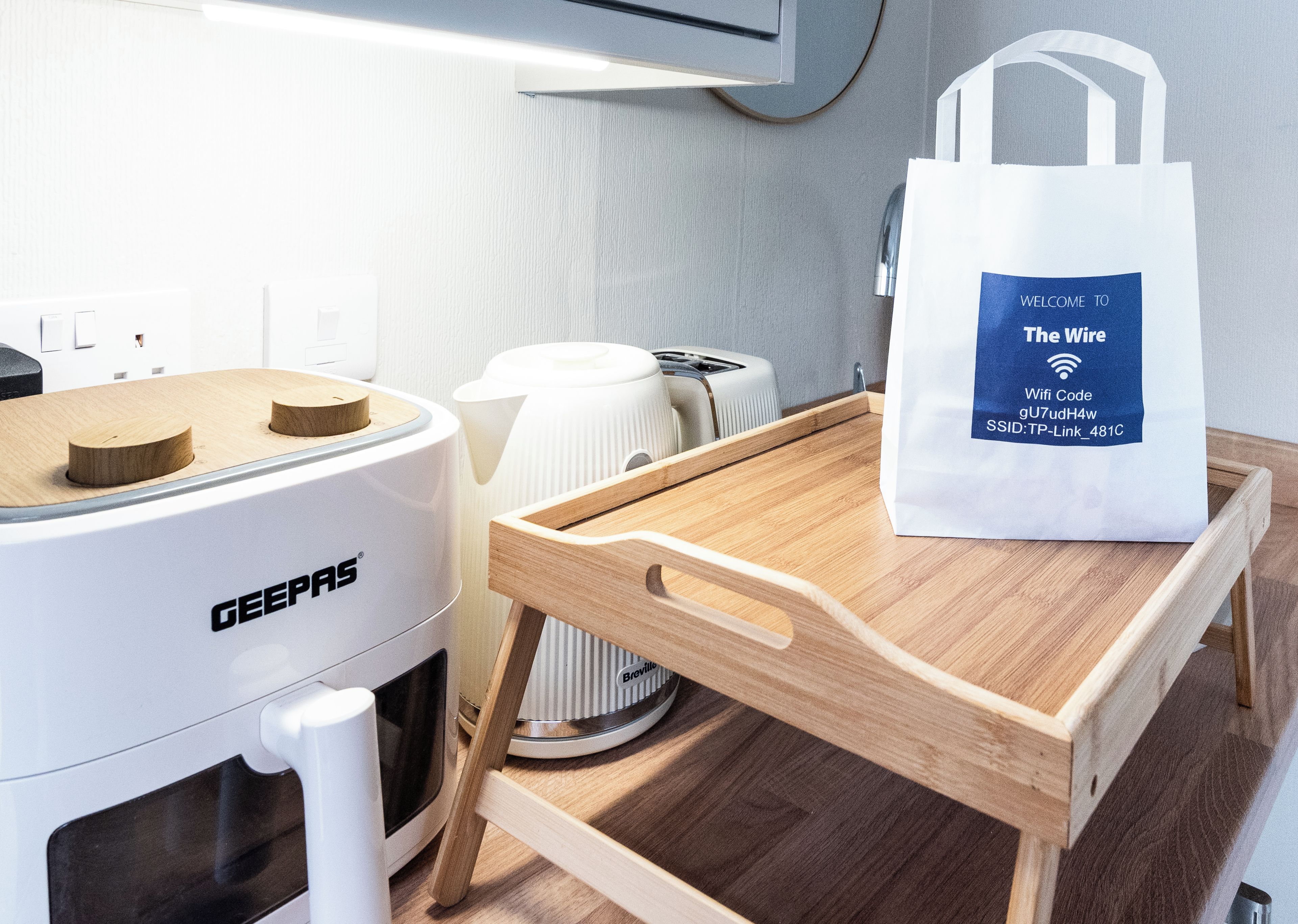 Eine Küchenzeile mit einer GEEPAS-Kaffeemaschine, einem Breville-Toaster und einer weißen Tasche mit WLAN-Code auf einem Holztischchen.