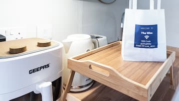 A kitchenette with a GEEPAS coffee machine, a Breville toaster, and a white tote bag with a WiFi code on a wooden tray table.