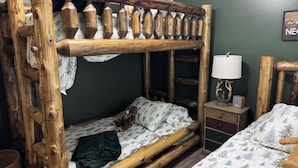 A bunk bed with a wooden ladder and a nightstand with a lamp and a clock.