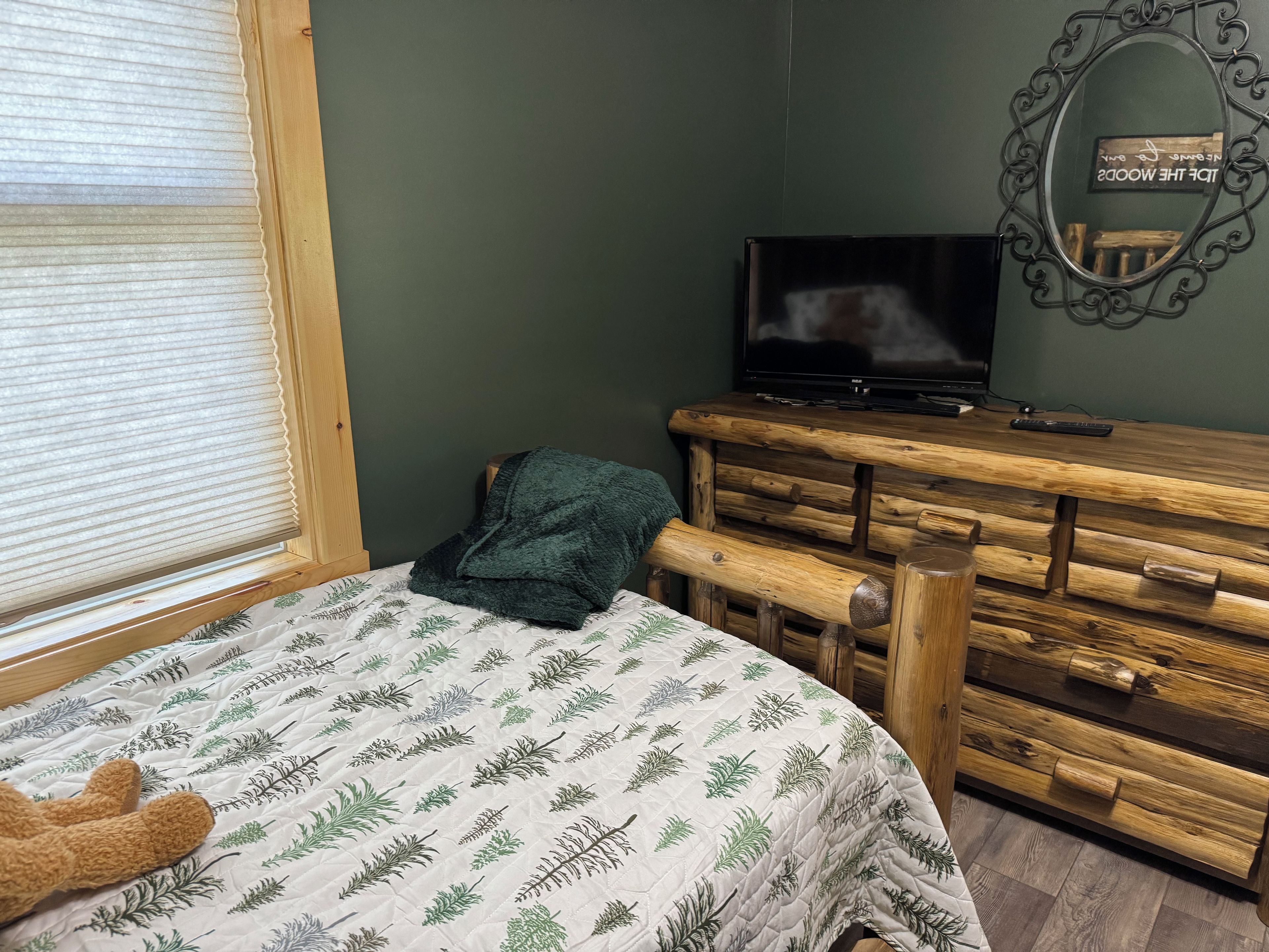 A bedroom with a bed, a dresser, a television, and a window with blinds.