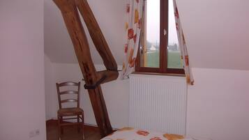 Une pièce avec un plafond en pente, une chaise en bois, un radiateur et une fenêtre avec des rideaux.