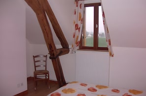 Une pièce avec un plafond en pente, une chaise en bois, un radiateur et une fenêtre avec des rideaux.