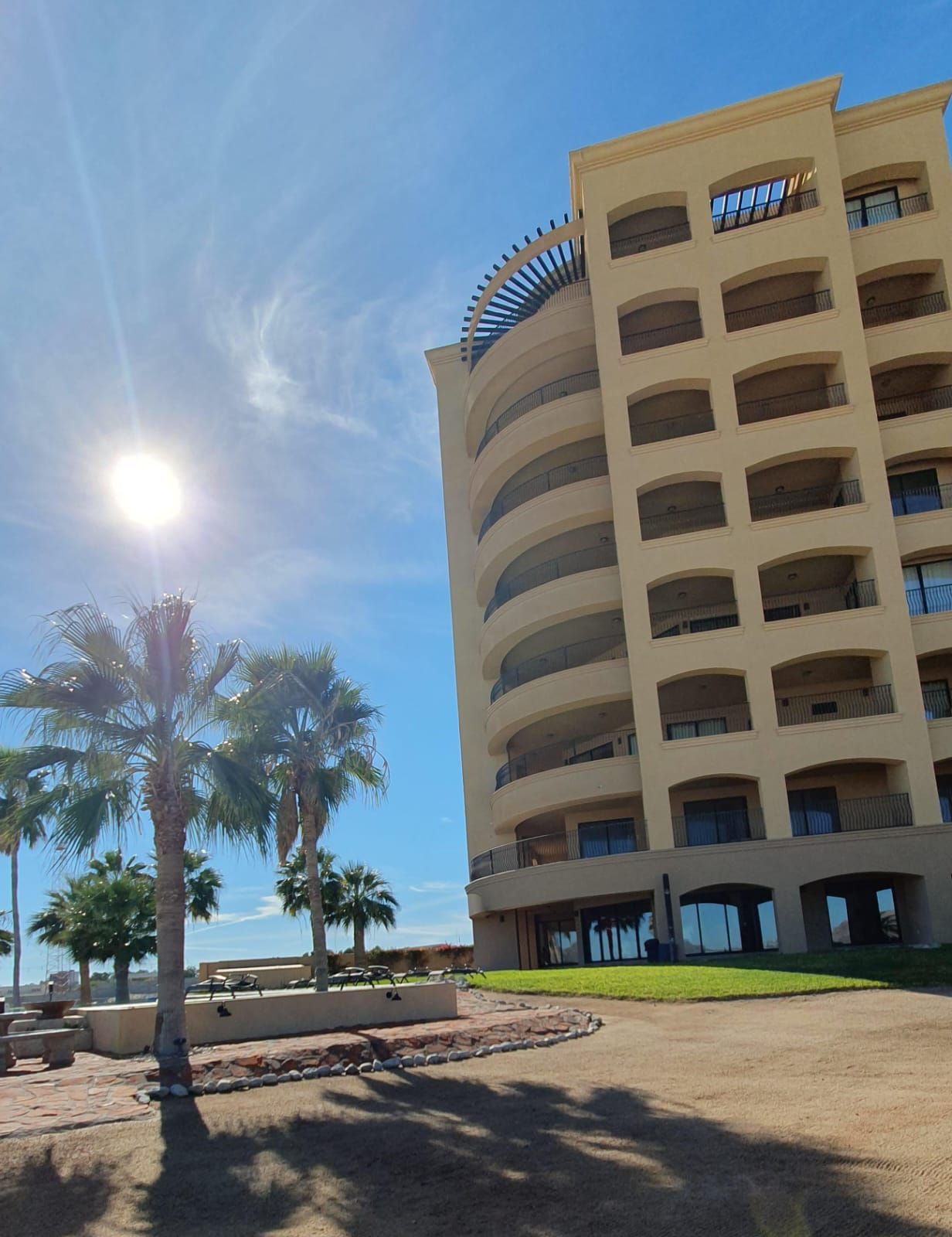 Un hotel de varios pisos con balcones, cielo despejado y palmeras.