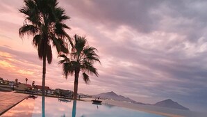 Una piscina con agua cristalina que refleja palmeras y un cielo al atardecer.